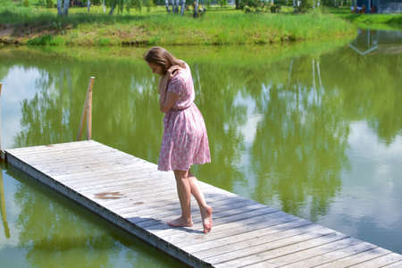 beautiful relaxed woman in pink dress on the pond in summer dreamingの写真素材