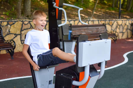 Boy athlete on outdoor sports ground. Child boy is exercising on the playground. Outdoor exercise machine for teenagers.の写真素材