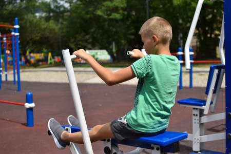 boy trains on the outdoor sports simulator. Sports child in the summer on playground. gymnastic exercises outside. boy overcoming efforts. achieve a difficult goal.の写真素材