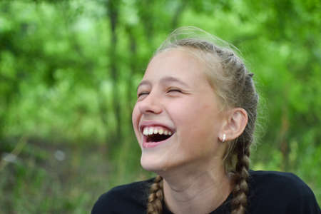 Happy girl laughs outdoors. Child teenager laughs outside in summer.