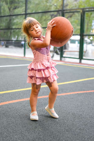 little child girl with basketball on the playground. Sporty child in a dress.の写真素材