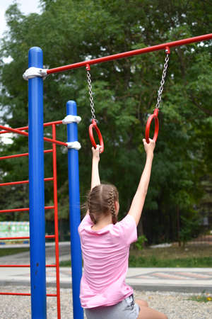 Child girl on outdoor athletic rings. outdoor. Child teenager girl goes in for sports on the street...