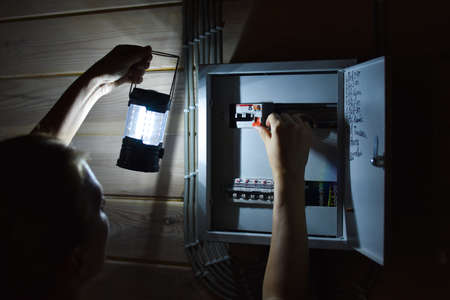 electrical panel with power buttons in house. In evening lights turned off. Woman looking for a...
