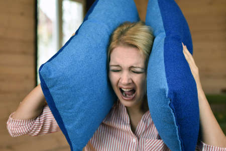 woman covered ears with pillow. Noisy neighbors make it difficult to live peacefully. woman was tired of loud neighbors and covered ears. Harmful neighbors.の写真素材