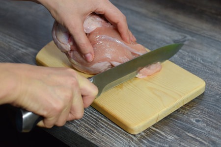 the cook cuts the meat in the kitchen. cooking meat dishes. woman cuts a piece of chicken meatの写真素材
