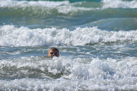 boy swims in sea in the waves. child is resting actively at sea on vacation