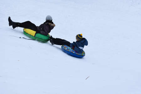 happy kids tubing down snow slide in winter. cheerful childrens active sports winter recreation. ice...