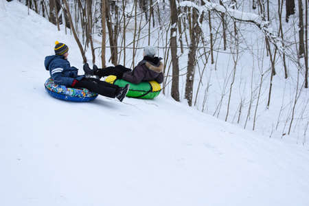 happy kids tubing down snow slide in winter. cheerful childrens active sports winter recreation. ice...