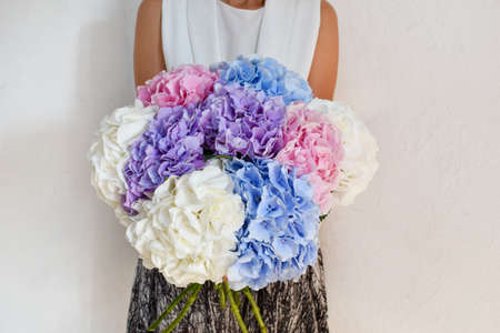 Woman with a bouquet of hydrangeas. Beautiful fresh delicate flowers for the holiday. Woman with beautiful flowers in her hands indoors background. Bouquet for a flower shop.の写真素材