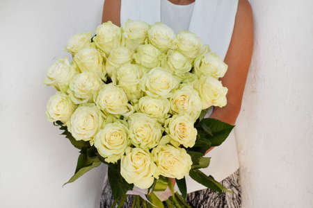 bouquet of fresh white high roses in the hands of woman. Beautiful fresh flowers for holiday. Woman with beautiful white flowers indoors.の写真素材