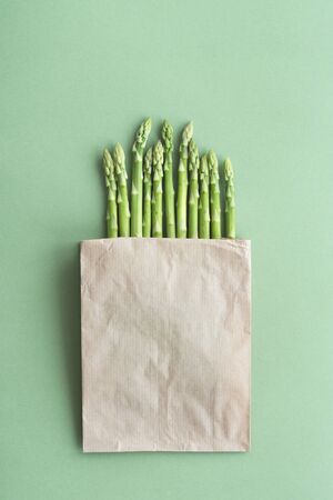 Freshly cut young asparagus packed in craft bag on a green background. Flat lay style.の写真素材