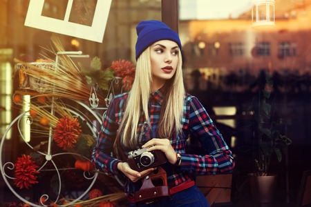 Portrait of beautiful young playful hipster woman with old retro camera. Model looking aside. City lifestyle. Toned.の写真素材