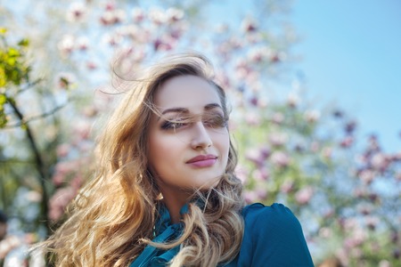 Outdoor portrait of a young beautiful happy smiling lady posing near magnolia tree with flowers. Model looking at camera. Girl wearing stylish clothes. Female spring fashionの写真素材