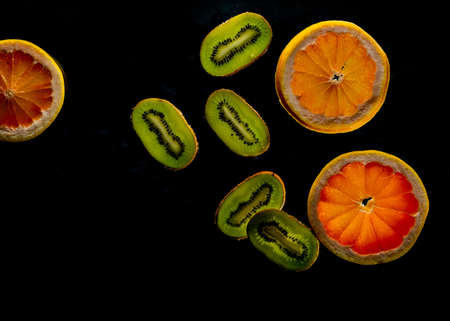 Sliced grapefruit, kiwi half isolated on black background. Pink,orange Kiwi, grapefruit citrus fruit, slice with zest, dramatic light texture, mixed colorful sliced fruits as background back lightedの写真素材