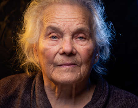 Portrait of beautiful elderly old woman in colorful bright lights blue and yellow, , 70s, grandmother, on black background., positive, smiling at camera, happy, studio, Close up, gray hair, caucasianの写真素材