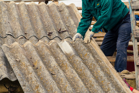 Risks nonProfessionals unprotected remove sheets of asbestos material from the roof of a rural home House with old, dangerの写真素材
