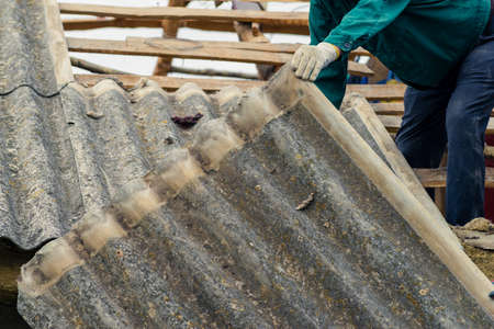Risks nonProfessionals unprotected remove sheets of asbestos material from the roof of a rural home House with old, dangerの写真素材