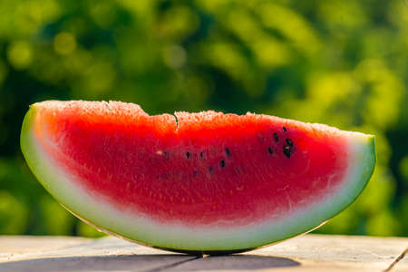 Delicious refreshing watermelon on the outdoors wooden table, GREEN natural background Slice sunny...