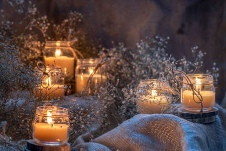 Wax handmade home-based Burning white candle in the jar coarse textile Vintage glow Flame dry bouquet gypsophila flower rustic dark mood orange blue lightの写真素材