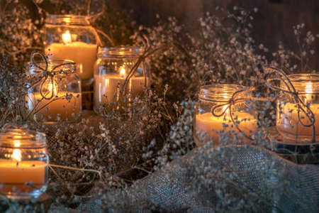 Wax handmade home-based Burning white candle in the jar coarse textile Vintage glow Flame dry bouquet gypsophila flower rustic dark mood orange blue lightの写真素材