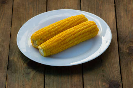 boiled corn on cobs white plate Fresh sweet on rustic wooden table, closeup, Cooked corn, Homemade...