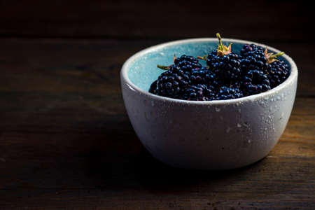 Ripe blackberries with leaves in a clay bowl on a wooden background dark food photography, Sweet tasty heap Antioxidant organic superfoodの写真素材