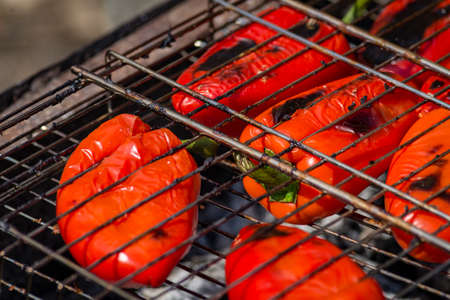 Grilling Process of preparing red bell pepper on barbecue bbq grill. Flaming fire, ember charcoal and smoke. Close up Whole street food picnic vegetables organicの写真素材