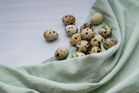 Fresh little quail eggs on white wooden background with space for text Easter banner, pastel green...