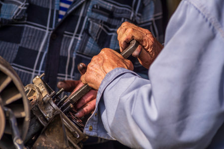 Two old men Auto mechanic working on car rusty engine in mechanics garage. Repair service close-up wrinkled dirty hands blue clothes Gear truck Disassemble wrench homeの写真素材
