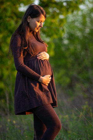 27 weeks Pregnant european with glasses woman tenderly hugs her belly surrounded by lilac flowers outside girl sunset Tummy new life concept brown drees springの写真素材