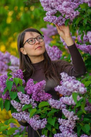 27 weeks Pregnant european with glasses woman tenderly hugs her belly surrounded by lilac flowers outside girl sunset Tummy new life concept brown drees springの写真素材