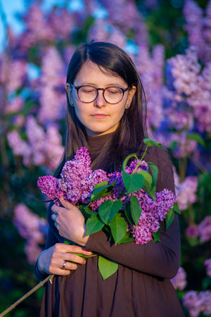 27 weeks Pregnant european with glasses woman tenderly hugs her belly surrounded by lilac flowers outside girl sunset Tummy new life concept brown drees springの写真素材