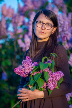 27 weeks Pregnant european with glasses woman tenderly hugs her belly surrounded by lilac flowers outside girl sunset Tummy new life concept brown drees springの写真素材