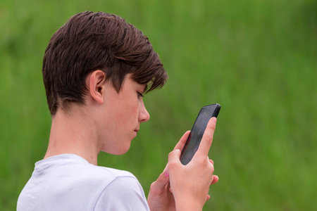 Teenage boy looking into a phone smartphone outdoors. Danger of internet green natural background natureの写真素材