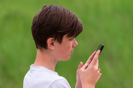 Teenage boy looking into a phone smartphone outdoors. Danger of internet green natural background natureの写真素材