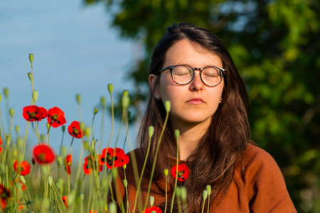 portrait of a beautiful young woman glasses holding bouquet of red poppies field cute brunette girl morning sun light nature romantic spring time Outdoor Freedom concept.の写真素材