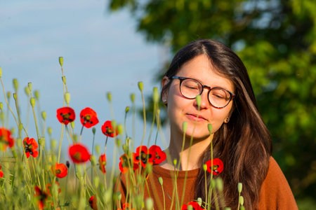 portrait of a beautiful young woman glasses holding bouquet of red poppies field cute brunette girl morning sun light nature romantic spring time Outdoor Freedom concept.の写真素材