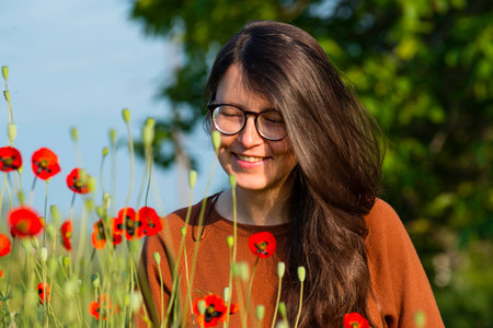 portrait of a beautiful young woman glasses holding bouquet of red poppies field cute brunette girl morning sun light nature romantic spring time Outdoor Freedom concept.の写真素材