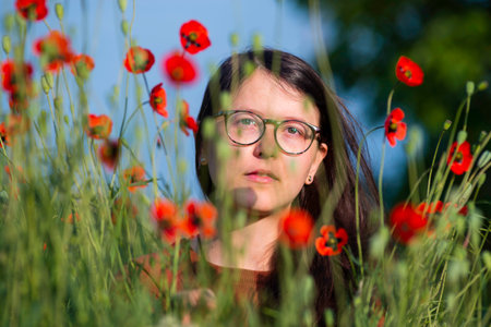 portrait of a beautiful young woman glasses holding bouquet of red poppies field cute brunette girl morning sun light nature romantic spring time Outdoor Freedom concept.の写真素材
