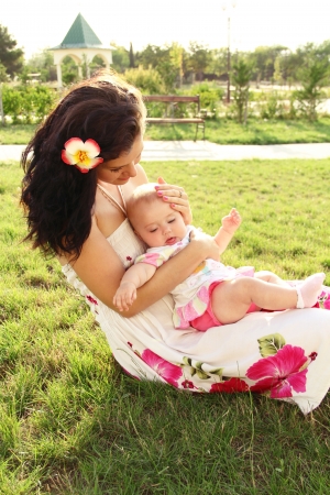 beautiful young mother with daughter relaxing sitting grass background summer meadow green grass treesの写真素材