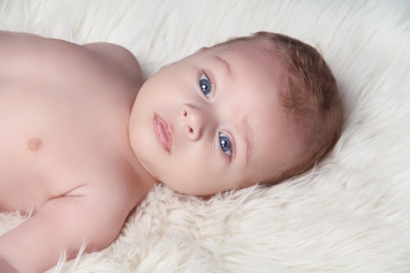 Looking baby lying on fur white bedの写真素材