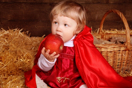 Little girl is sitting on pile of straw eating appleの写真素材