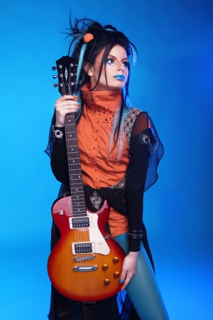 Rock girl posing with electric guitar isolated on blue backgroundの写真素材