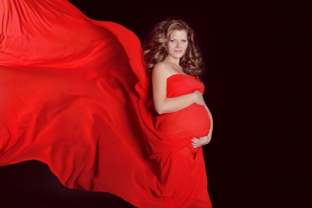 Beautiful Pregnant woman stroking her belly with red blowing tissue isolated on black backgroundの写真素材