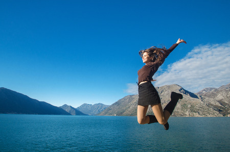 Beautiful Jumping Girl enjoying nature with her opened arms over blue sky, mountains. Free Happy Woman. Elated by successの写真素材