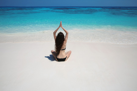 Young woman practicing yoga on the exotic beach with blue water and white sand. Relax. Meditation, peace. Balance. Bliss freedom concept.の写真素材