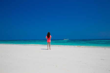 Beautiful woman walking on exotic beach, brunette girl model in red dress on the ocean coast. Vacation. Travel. Bliss freedom concept.の写真素材