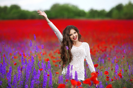 Beautiful young woman portrait in poppies field. Attractive brunette girl with long curly hair style in white dress walking and dreaming. Wellness. Lifestyle.の写真素材