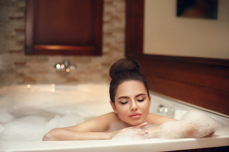 Young woman relaxing in foam hot tub bath spa, brunette enjoying the aromatherapy in wellness center. Beautiful model in luxury spa resort. Beauty skin care treatment.の写真素材