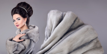 Fashion photo of woman in mink fur coat. Elegant brunette with makeup, hairstyle, manicured nails. Glamour female wearing Siberian sable isolated on grey background.の写真素材